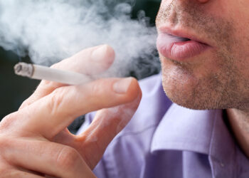 A closeup of a man breathing out the cigarettes' smoke