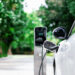 Focus closeup electric vehicle plugged in with EV charger device from blurred background of public charging station powered by renewable clean energy for progressive eco-friendly car concept.